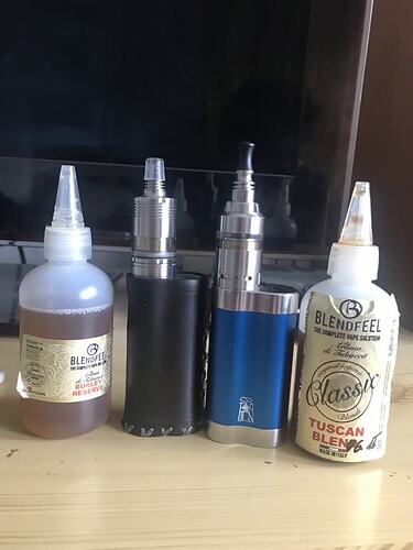 Két elektromos cigaretta készülék és két üveg e-folyadék egy asztalon egy TV előtt elhelyezve. (Feliratozva AI-val)