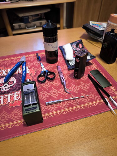 Sur la table, divers accessoires de vape, appareils et liquides sont disposés sous un textile à motifs rouges. (Légendé par IA)