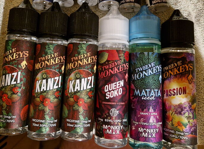 In the picture, six different flavored Twelve Monkeys and Monkey Mix e-liquid bottles are visible side by side. (Captioned by AI)