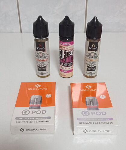On the table are three different vape e-liquid bottles and two Geekvape Q Pod cartridges. (Captioned by AI)