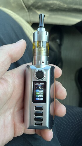 Egy kéz egy ezüst színű elektronikus cigarettát (vape) tart, melynek kijelzőjén különböző beállítások láthatók. (Feliratozva AI-val)