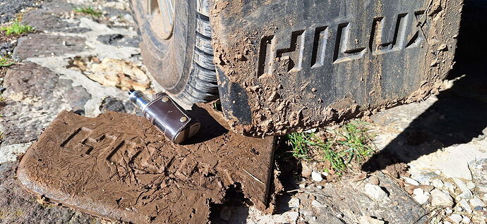 The image shows a dirty tire track with the inscription "HILUX", and next to it, a rain-droplet sticker is on the ground. (Labeled by AI)