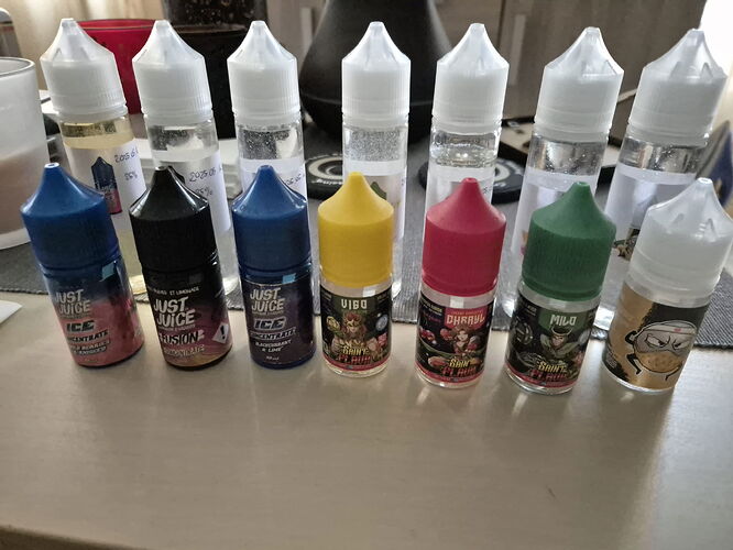 Az asztalon különböző márkájú és színű Just Juice e-liquid üvegek sorakoznak egymás mellett. (Feliratozva AI-val)