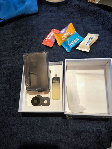 The picture shows an open box, containing a small plastic tank, some round parts, and items with colorful packaging. (Labeled by AI)