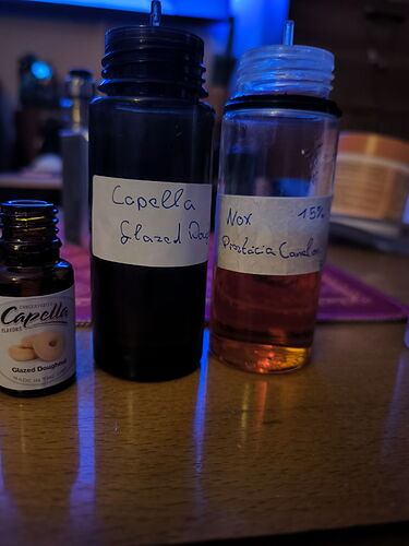 Trois flacons de différentes tailles et conceptions, étiquetés à la main et contenant des liquides, sont posés sur la table. (Étiqueté par IA)