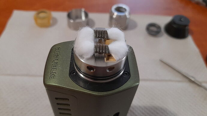 The image shows a vape atomizer with sponge-like cotton and a dual heating wire on a green Republic brand e-cigarette device, with various parts in the background. (Subtitled by AI)