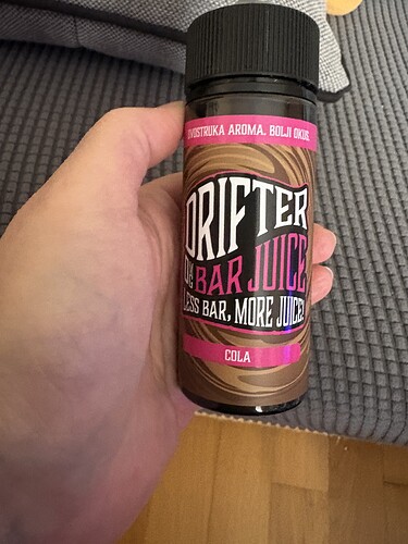 A képen egy "Drifter Bar Juice" nevű üveg látható, amely a "Cola" ízű italt tartalmazza, és egy kézben van. (Feliratozva AI-val)