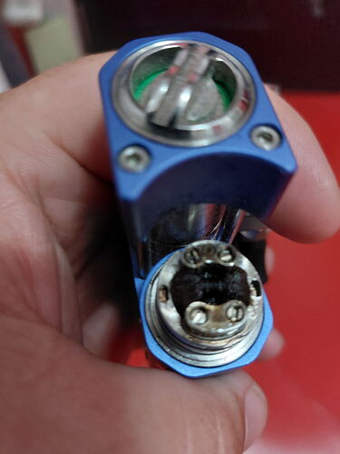 Une partie d'un appareil électronique bleu tenue dans une main, montrant une pièce métallique vissée attachée à une section cylindrique. (Légendé par IA)