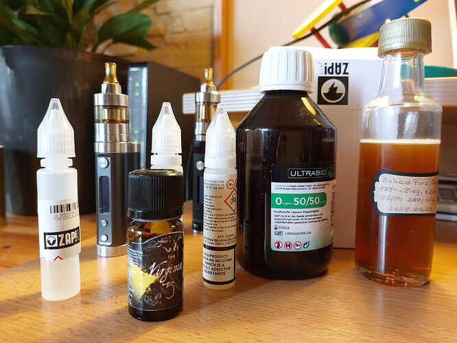 Az ábrán különböző e-cigaretták és folyadékok láthatók, beleértve az ízesített nikotintartalmú folyadékokat is. (Feliratozva AI-val)