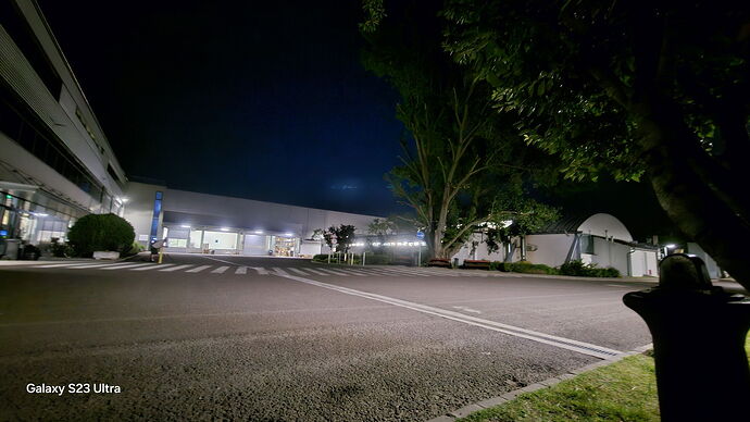 La photo de nuit montre un parking vide et un bâtiment moderne, bien éclairé, entouré d'arbres. (Légendé par IA)