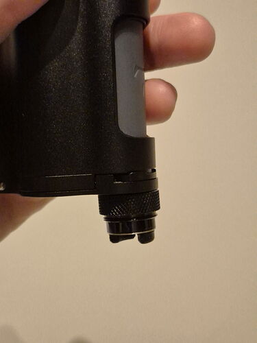 Une main tenant un appareil cylindrique noir, probablement technique, avec deux petites lentilles ou capteurs ronds à sa base. (Légendé par IA)