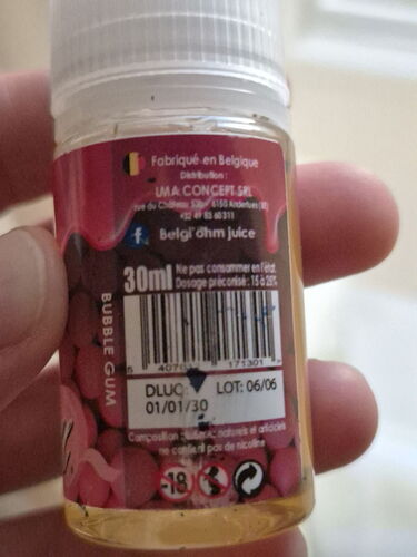 A 30ml bottle of e-liquid from Belgium held in a hand, with proper usage and safety information on its label. (Auto-captioned)