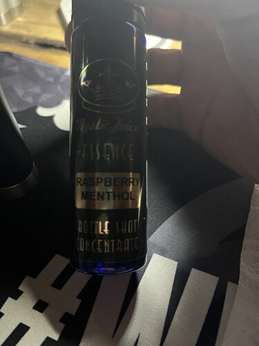 On the image is a dark blue bottle, which reads 'Raspberry Menthol' and 'Bottle Shot Concentrate'. (Captioned by AI)