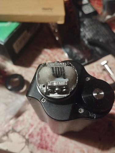 An electronic cigarette atomizer with cotton placed inside it, among various items on a table. (Captioned by AI)