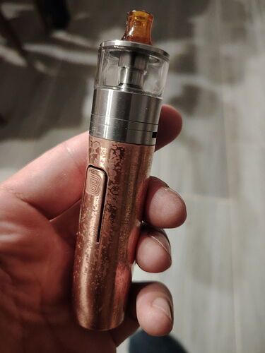 Cigarette électronique (vape) cuivrée et à texture métallique, tenue dans une main. (Légendé par IA)