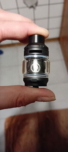 A hand holds a small, black and clear vape tank between two fingers. (Labeled by AI)