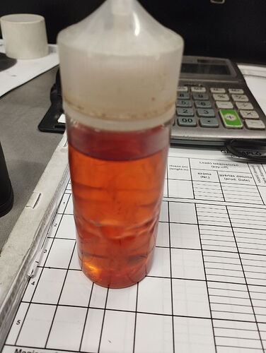 A reddish liquid in a plastic bottle, placed on a table full of papers and a calculator. (Caption by AI)