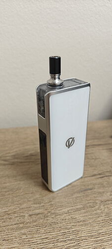 In the picture, a white, rectangular electric cigarette (vape) with a metal edge is visible on a wood-patterned table, against a neutral background. (Labeled by AI)
