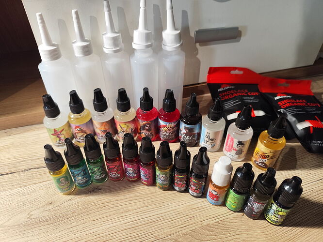 Sur la table, des encres ou liquides de différentes tailles et couleurs sont disposés dans différentes bouteilles en plastique et flacons compte-gouttes. (Sous-titré par IA)