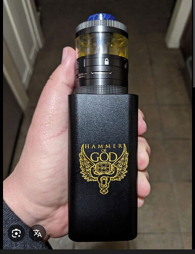 Une personne tenant un appareil de vapotage noir, avec un logo doré 'HAMMER OF GOD' et un réservoir transparent rempli d'un liquide jaune. (Légendé par IA)