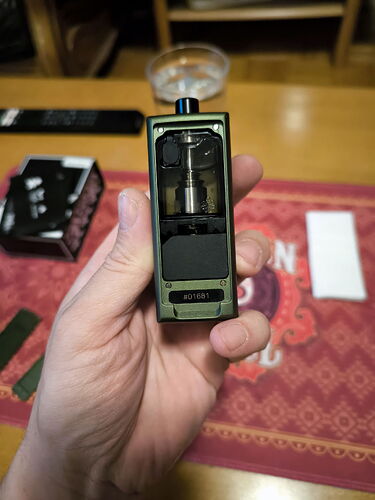 A green vaporizer is shown in the image, held by a hand, with various objects in the background. (Autogenerated by AI)