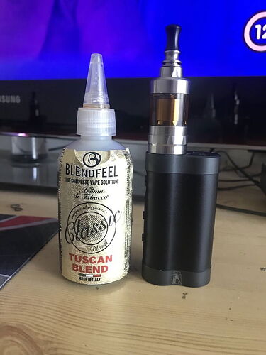 Az asztalon egy Blendfeel Tuscan Blend e-liquid és egy fekete elektromos cigaretta (vape) készülék található. (Feliratozva AI-val)