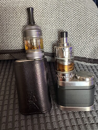 Deux dispositifs de cigarette électronique différents sont placés sur une surface grise. (Légendé par IA)