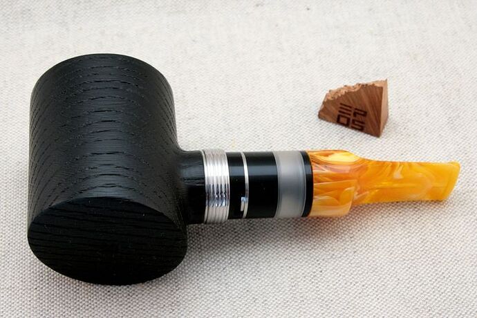 Egy fekete fa pipa, ezüst díszítéssel és átlátszó narancssárga szipkával egy világos szövetszöveten. (Feliratozva AI-val)