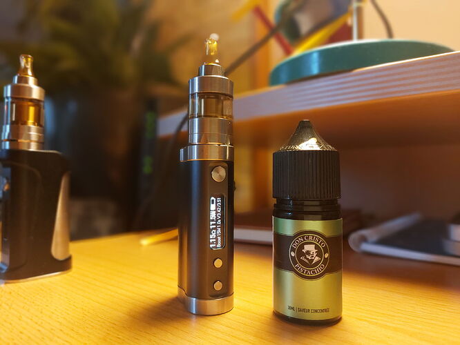 The picture shows two vape devices: a metal vape and a bottle of liquid, with another vape in the background. (Labeled by AI)