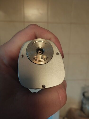 Une main tient un appareil métallique argenté, surmonté d'une pièce circulaire à visser. (Sous-titré par IA)