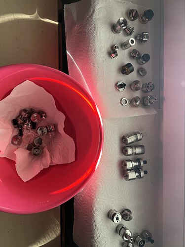 Le seau rouge et la table sont visibles sur l'image, disposant de divers manchons de verrouillage central métalliques et adaptateurs sur du papier essuie-tout blanc. (Légendé par IA)