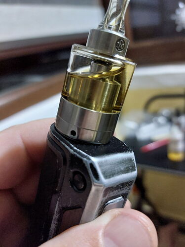 The image shows a vape device with golden yellow liquid in its tank, while a hand is holding it. (Labeled by AI)