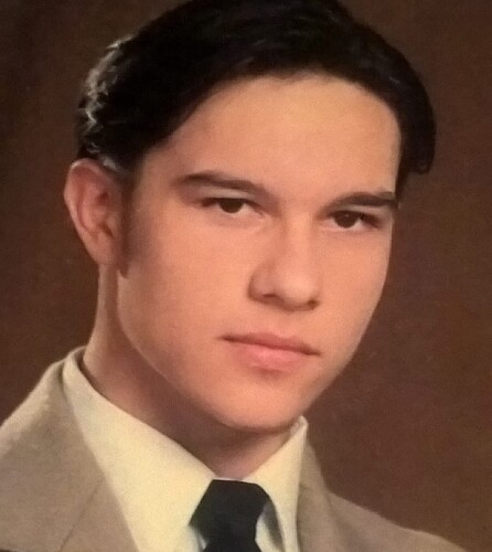 Portrait of a young man wearing a suit and tie and looking at the camera with a serious expression. (Captioned by AI)