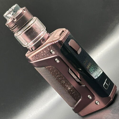 Un appareil e-cigarette brun métallique sur fond noir, avec un écran numérique et un réservoir transparent. (Légendé par IA)