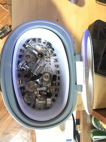 L'image représente un nettoyeur à ultrasons contenant diverses pièces métalliques et en plastique. (Légendé par IA)