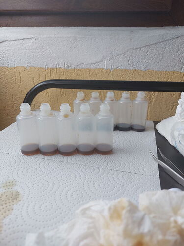 A képen egy sor átlátszó palack látható, amelyekben barna folyadék található, egy papírtörlőn elhelyezve. (Feliratozva AI-val)