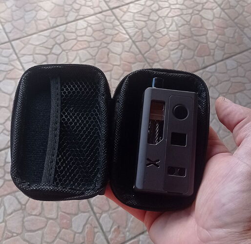 Egy kéz egy kis fekete cipzáras tokot tart, amelyben egy fekete elektronikus eszköz van elhelyezve. (Feliratozva AI-val)