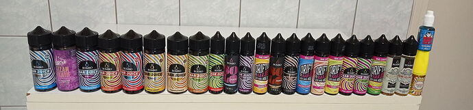 Egy sor vegyes ízű Bombo és Driptae vape juice palackok egy polcon egy fürdőszobai csempe mögött. (Feliratozva AI-val)