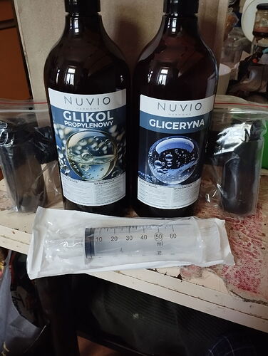 Deux grandes bouteilles, un glycol et une glycérine, ainsi qu'une grande seringue stérile placés dans un sac séparé, disposés sur une table. (Légendé par IA)