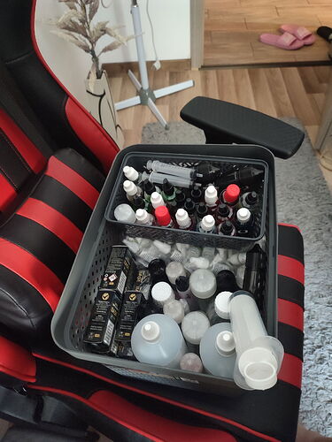 Une boîte contenant divers flacons de vernis à ongles et de produits cosmétiques est placée sur l'assise d'une chaise rouge et noire. (Intitulé par IA)