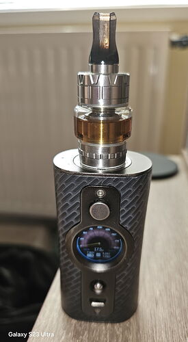 Cette image représente un appareil e-cigarette noir à motif de fibre de carbone, montrant des détails sur son écran et son réservoir. (Légendé par IA)