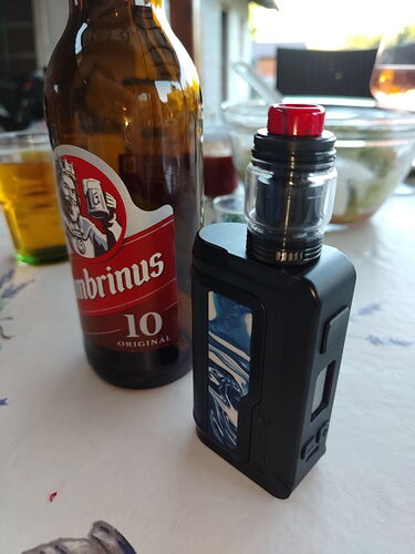 Egy asztalon egy barna Gambrinus sörösüveg és egy fekete elektromos cigaretta látható. (Feliratozva AI-val)