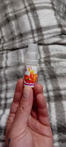 Une main tenant une petite bouteille en plastique d'arôme ou de concentré de boisson gazeuse, avec une couverture à carreaux en arrière-plan. (Traduit automatiquement par IA)