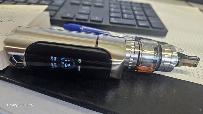 A silver vape device lies on a table, with a keyboard and a pen in the background. (AI-generated caption)