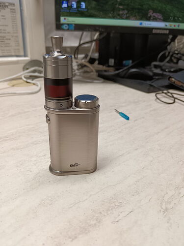 On the desk is a silver e-cigarette (vape) in front of a computer monitor and keyboard. (Captioned by AI)