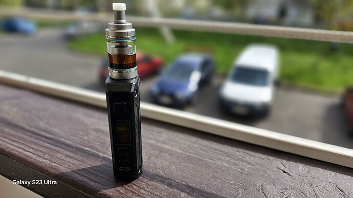 A modern vape device is shown, standing on a windowsill in front of parked cars. (Caption by AI)