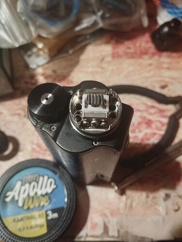 An electronic cigarette in an assembly state, with a box of Apollo wicking wire next to it, on a table. (Captioned by AI)