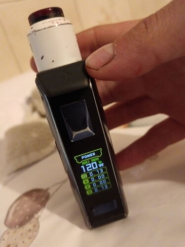 Egy kéz egy fekete elektromos cigaretta modult tart, amelyen 120 watt teljesítmény látható a kijelzőn. (Feliratozva AI-val)