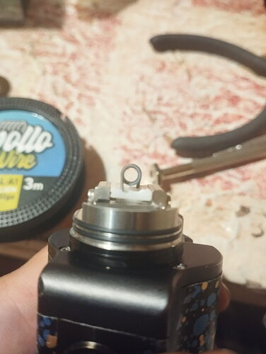 An electronic cigarette atomizer held by a hand, with an air gap at the top, a measuring tape and pliers are visible in the background. (Captioned by AI)