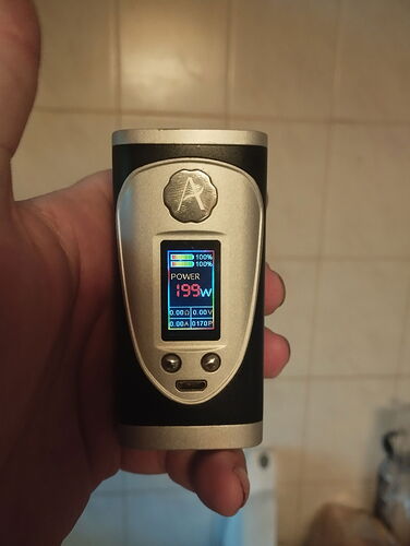 Une main tient un appareil électronique noir et argenté, avec un écran numérique couleur affichant diverses données de mesure et la mention "POWER 199W". (Sous-titré par IA)